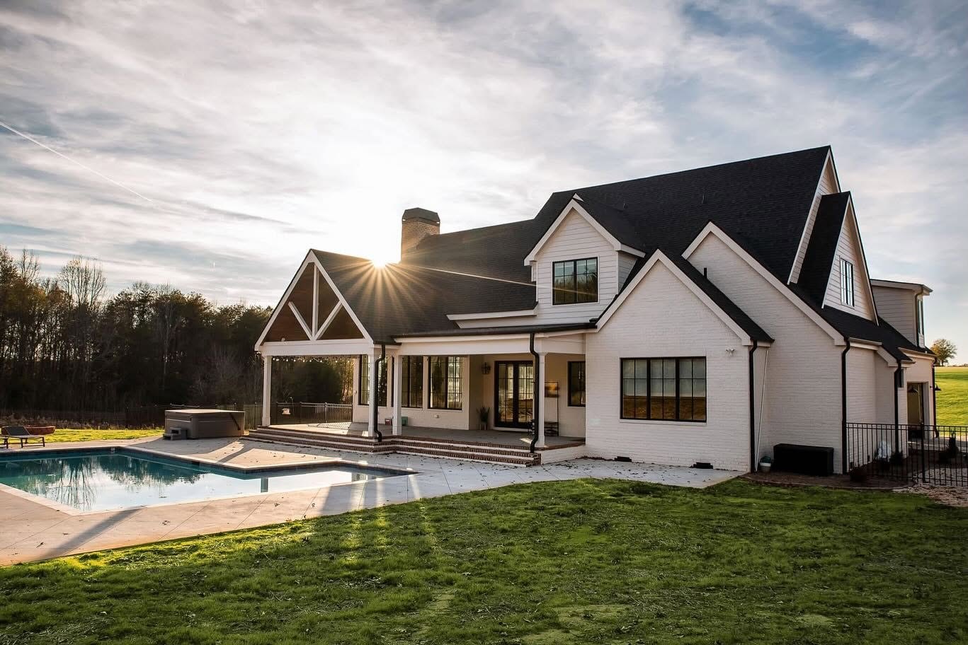 White brick home with dark gutters and a covered porch beside a pool at sunset